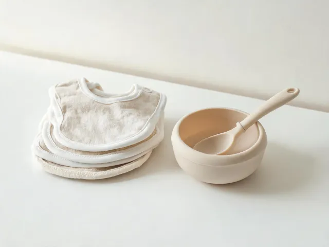 Minimal baby bibs stacked beside feeding bowl